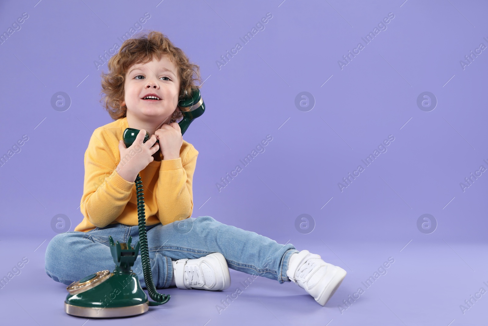 Photo of Cute little boy with old telephone on violet background, space for text