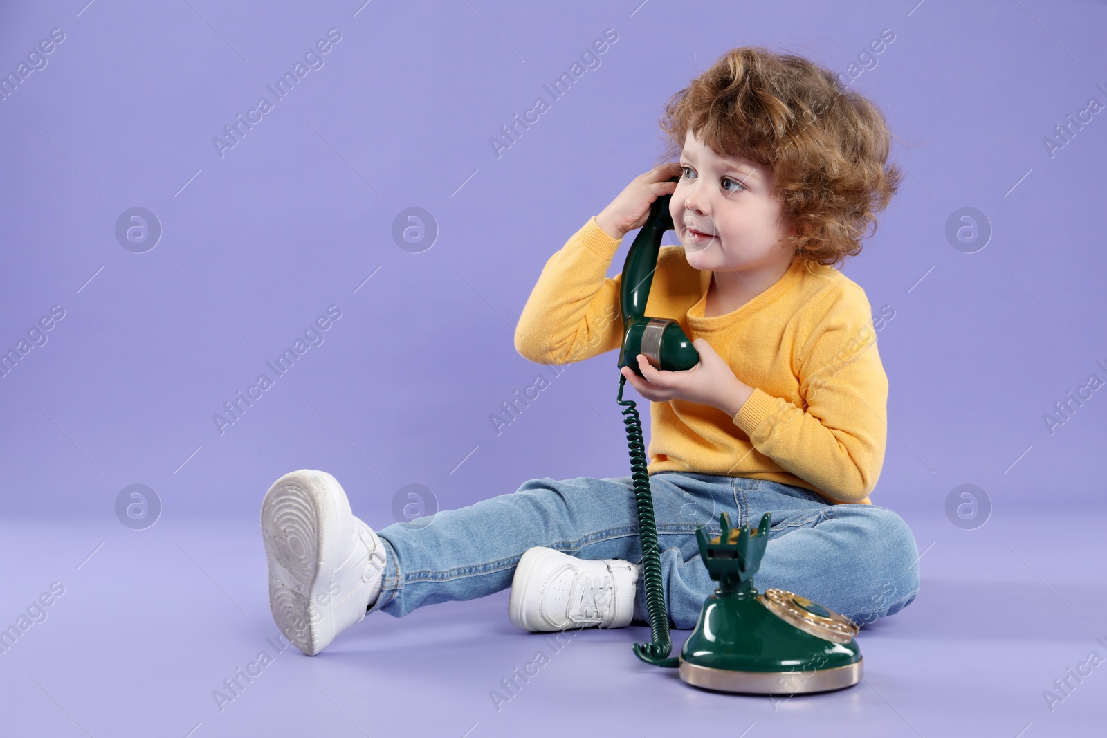 Photo of Cute little boy with old telephone on violet background