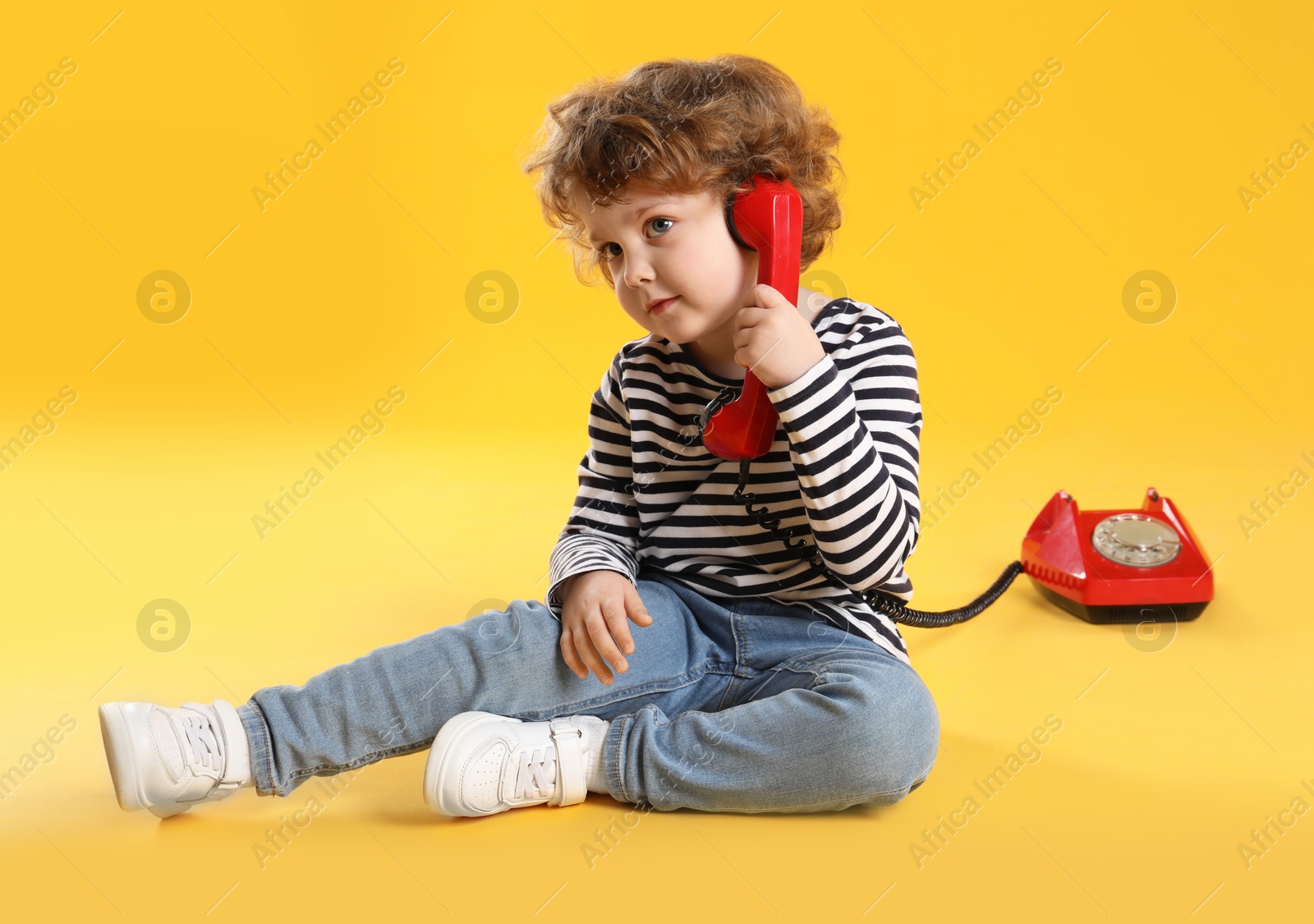 Photo of Cute little boy with telephone on orange background