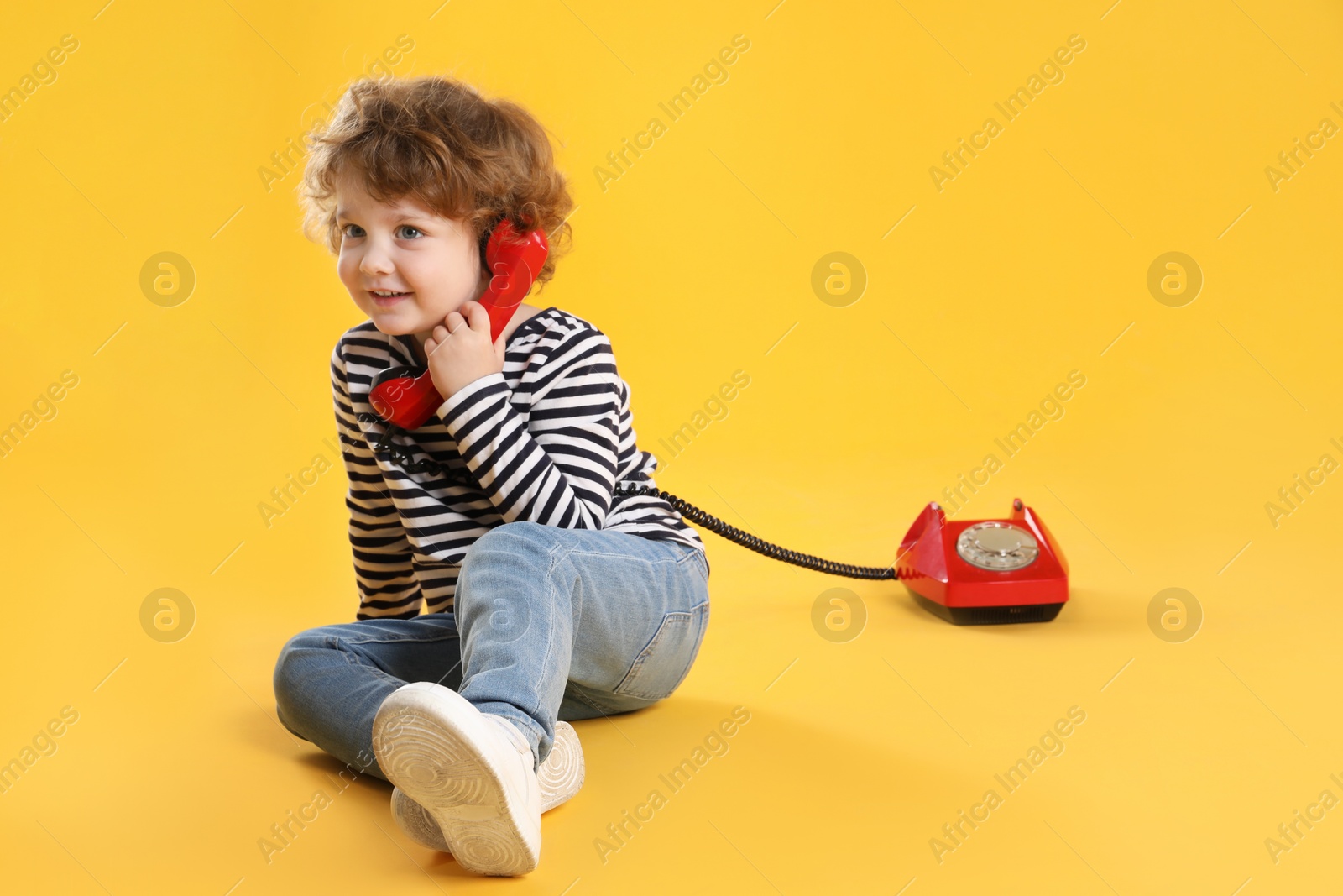 Photo of Cute little boy with telephone on orange background