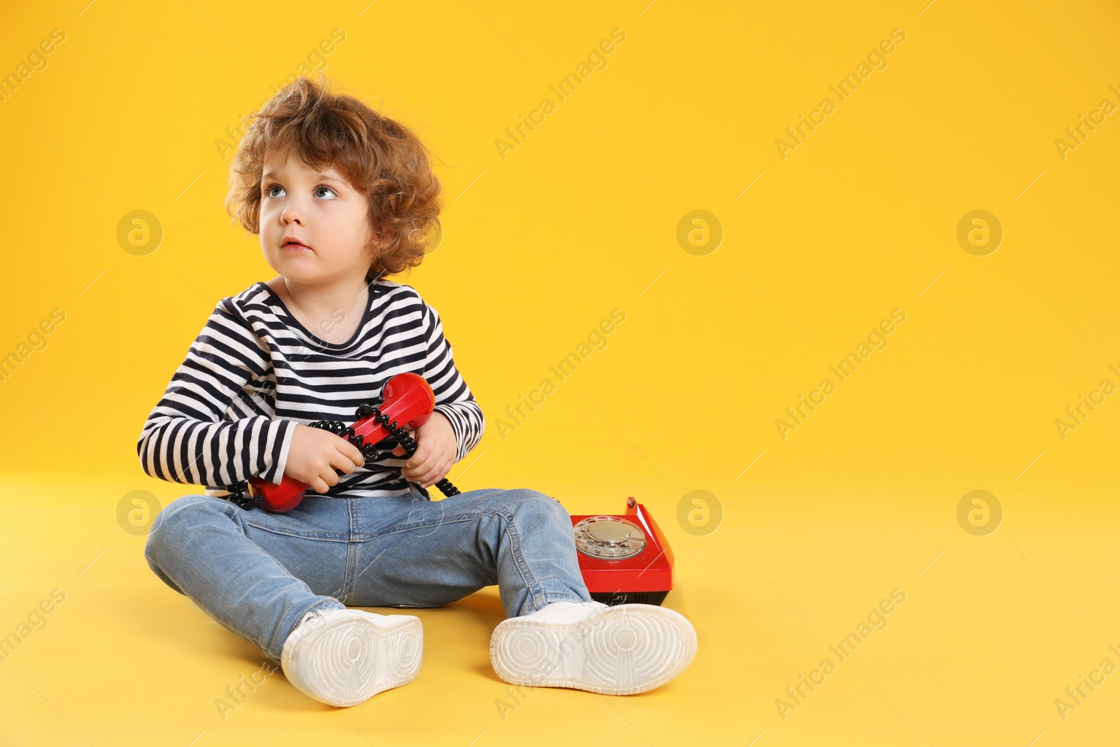 Photo of Cute little boy with telephone on orange background, space for text