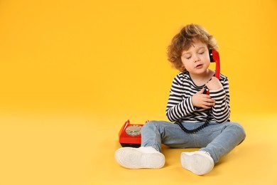 Photo of Cute little boy with telephone on orange background, space for text