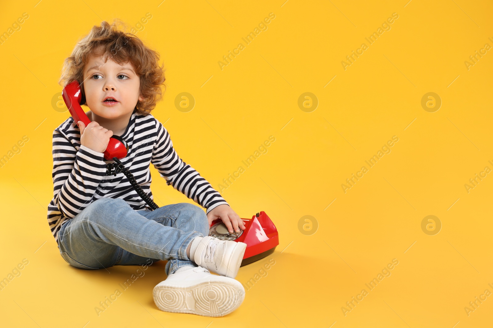 Photo of Cute little boy with telephone on orange background, space for text