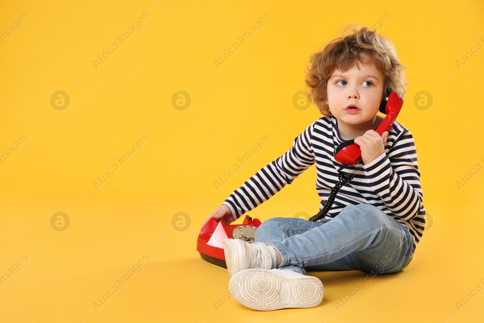 Photo of Cute little boy with telephone on orange background, space for text