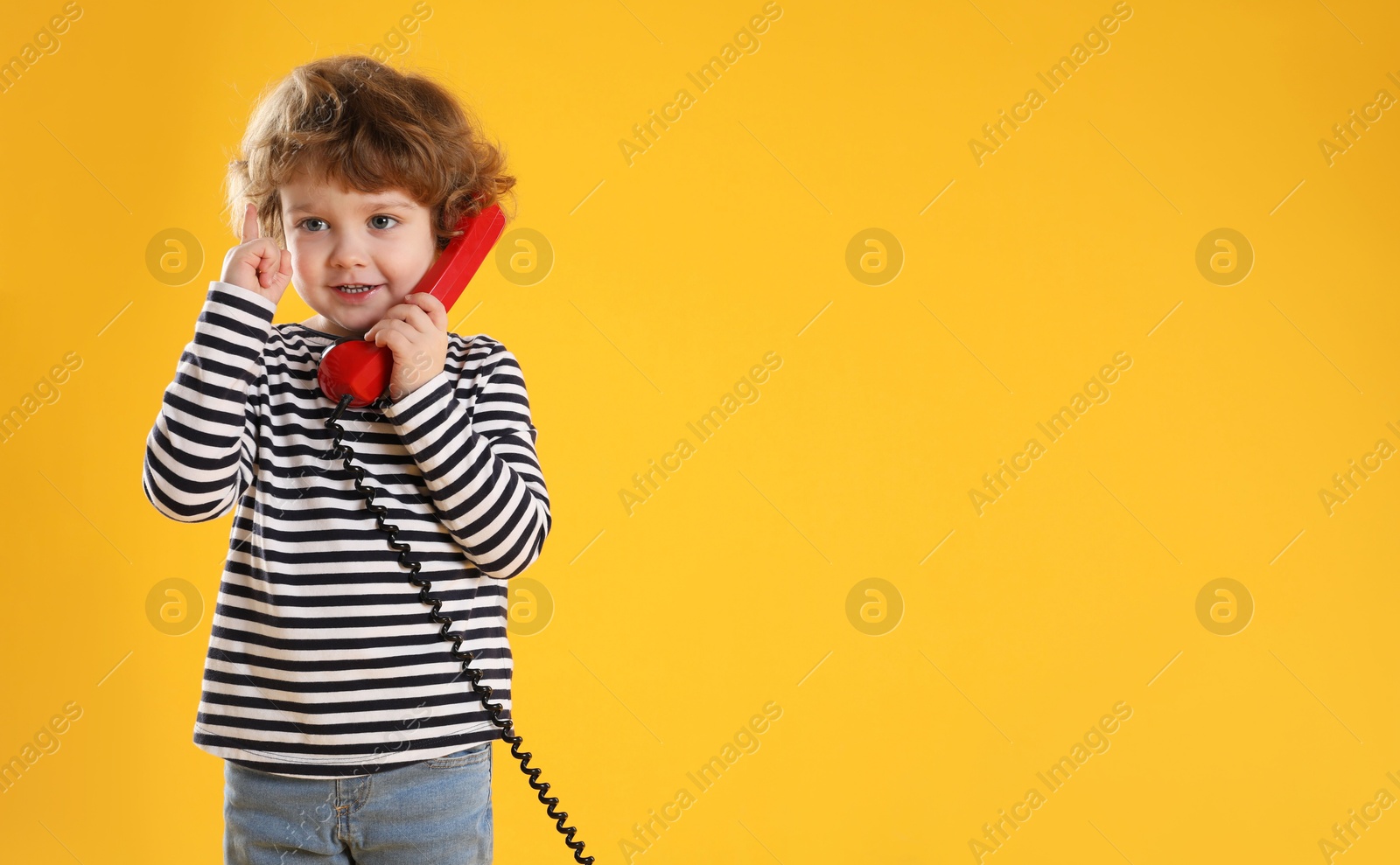 Photo of Cute little boy with telephone handset on orange background, space for text