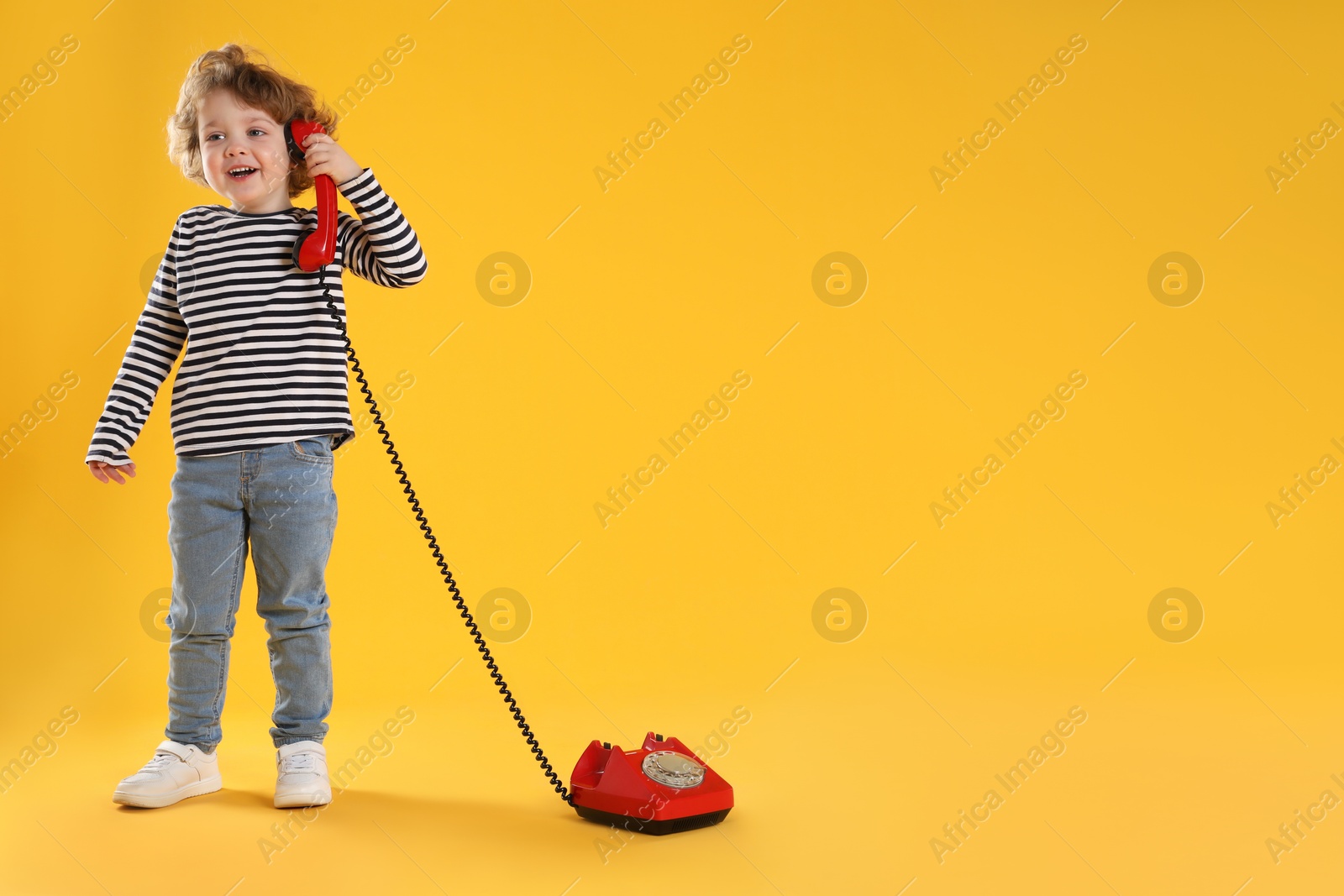 Photo of Cute little boy with telephone on orange background, space for text