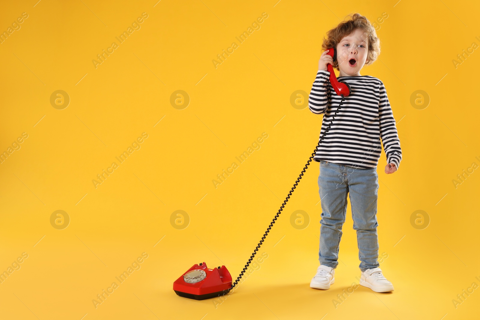 Photo of Cute little boy with telephone on orange background, space for text