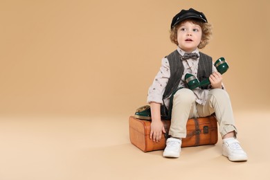 Photo of Cute little boy with old telephone and suitcase on beige background, space for text