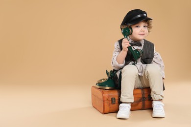 Photo of Cute little boy with old telephone and suitcase on beige background, space for text