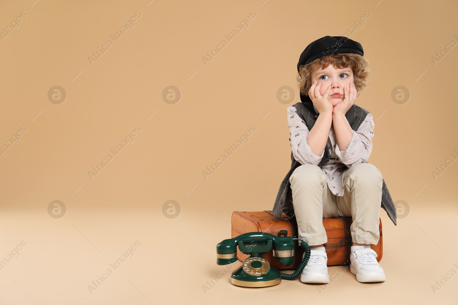 Photo of Cute little boy with old telephone and suitcase on beige background, space for text