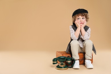 Photo of Cute little boy with old telephone and suitcase on beige background, space for text