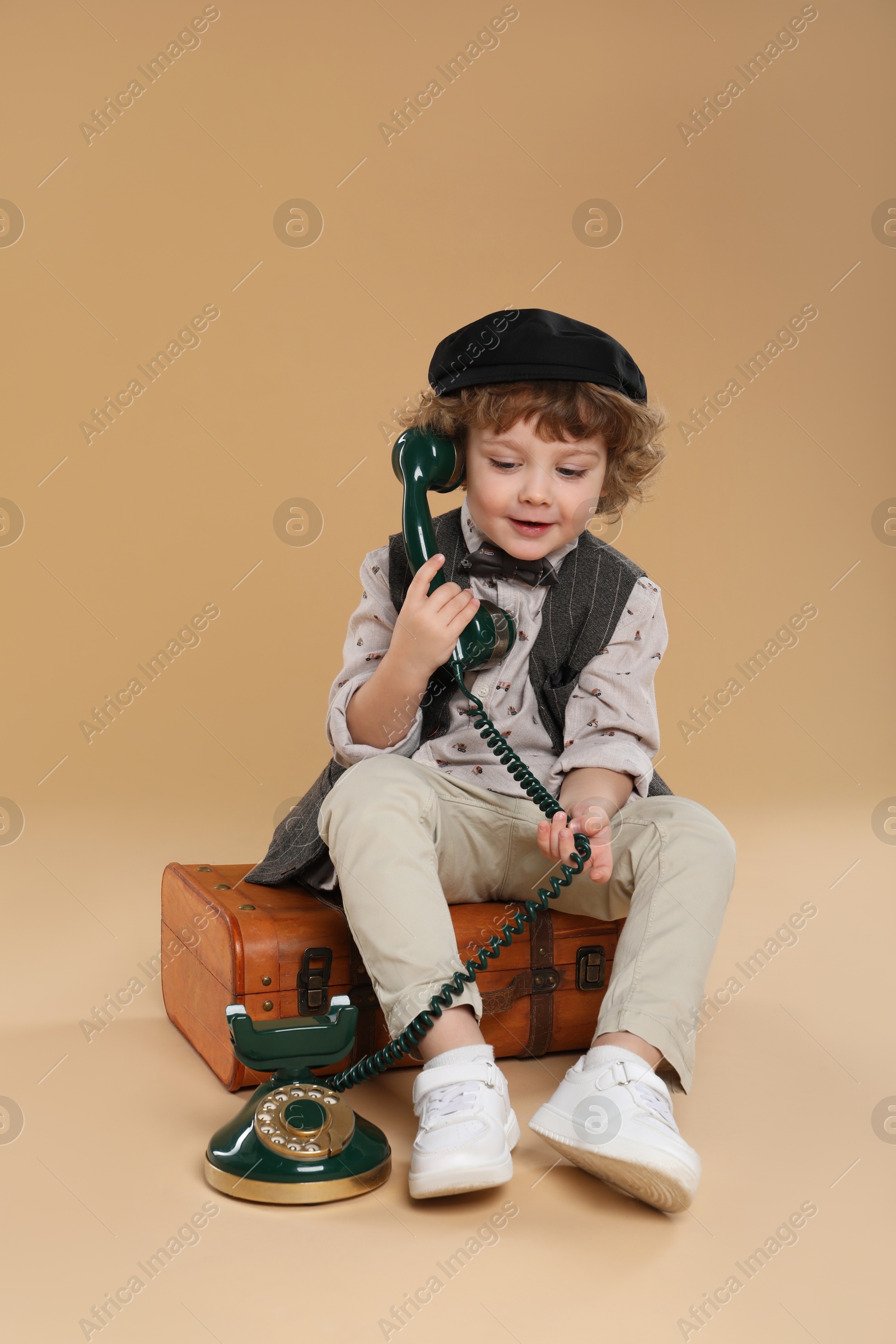 Photo of Cute little boy with old telephone and suitcase on beige background