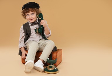 Photo of Cute little boy with old telephone and suitcase on beige background, space for text