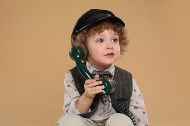 Photo of Cute little boy with telephone handset on beige background