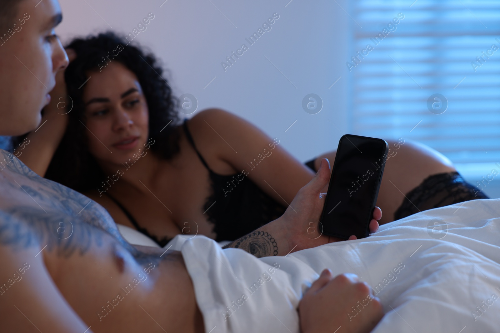 Photo of Betrayal. Man with smartphone and his mistress on bed, closeup