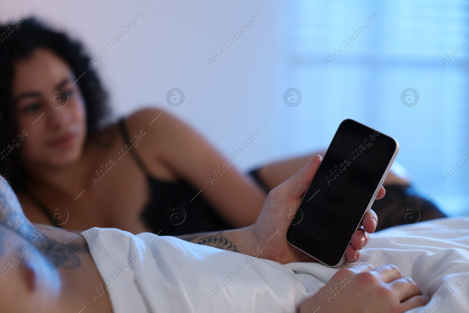 Photo of Betrayal. Man with smartphone and his mistress on bed, closeup