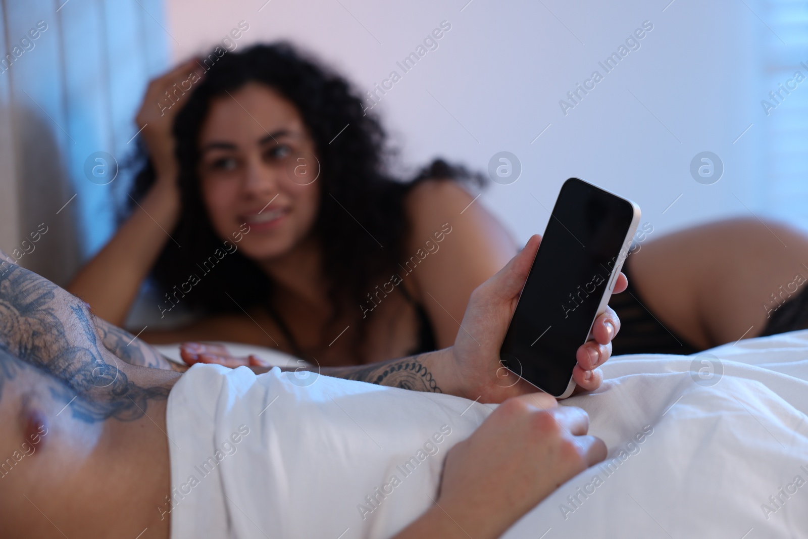 Photo of Betrayal. Man with smartphone and his mistress on bed, closeup