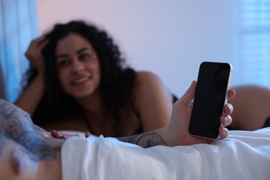 Photo of Betrayal. Man with smartphone and his mistress on bed, closeup