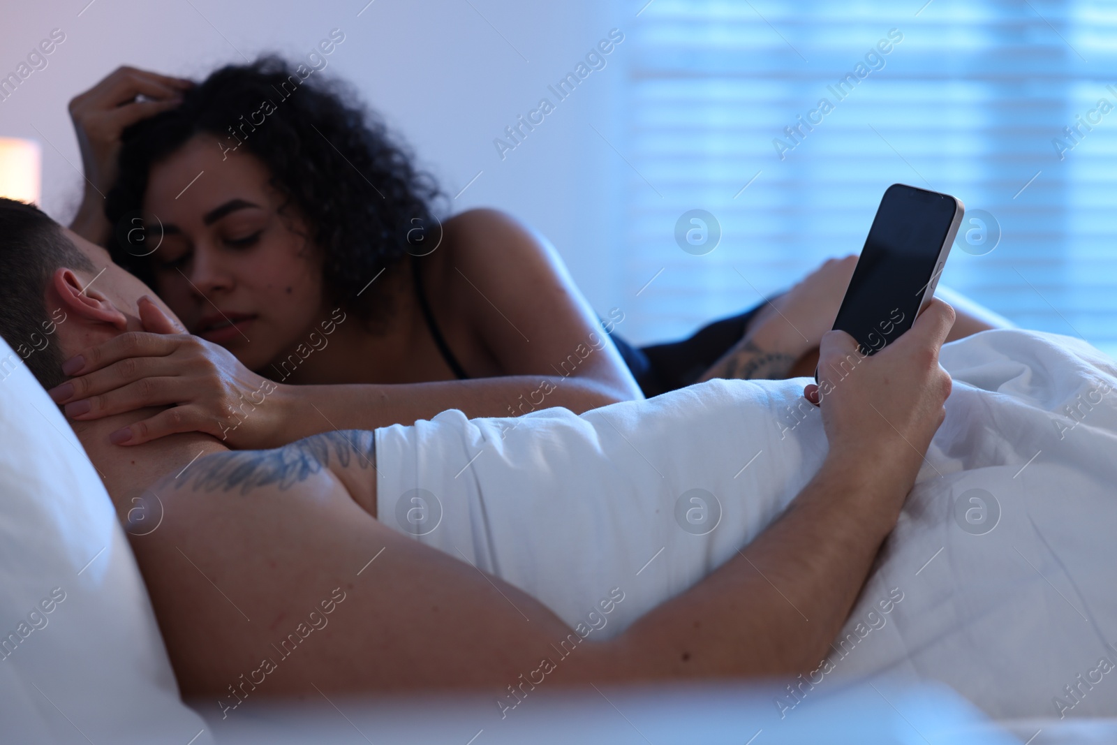 Photo of Betrayal. Man with smartphone and his mistress on bed