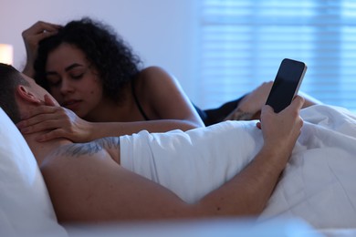 Photo of Betrayal. Man with smartphone and his mistress on bed