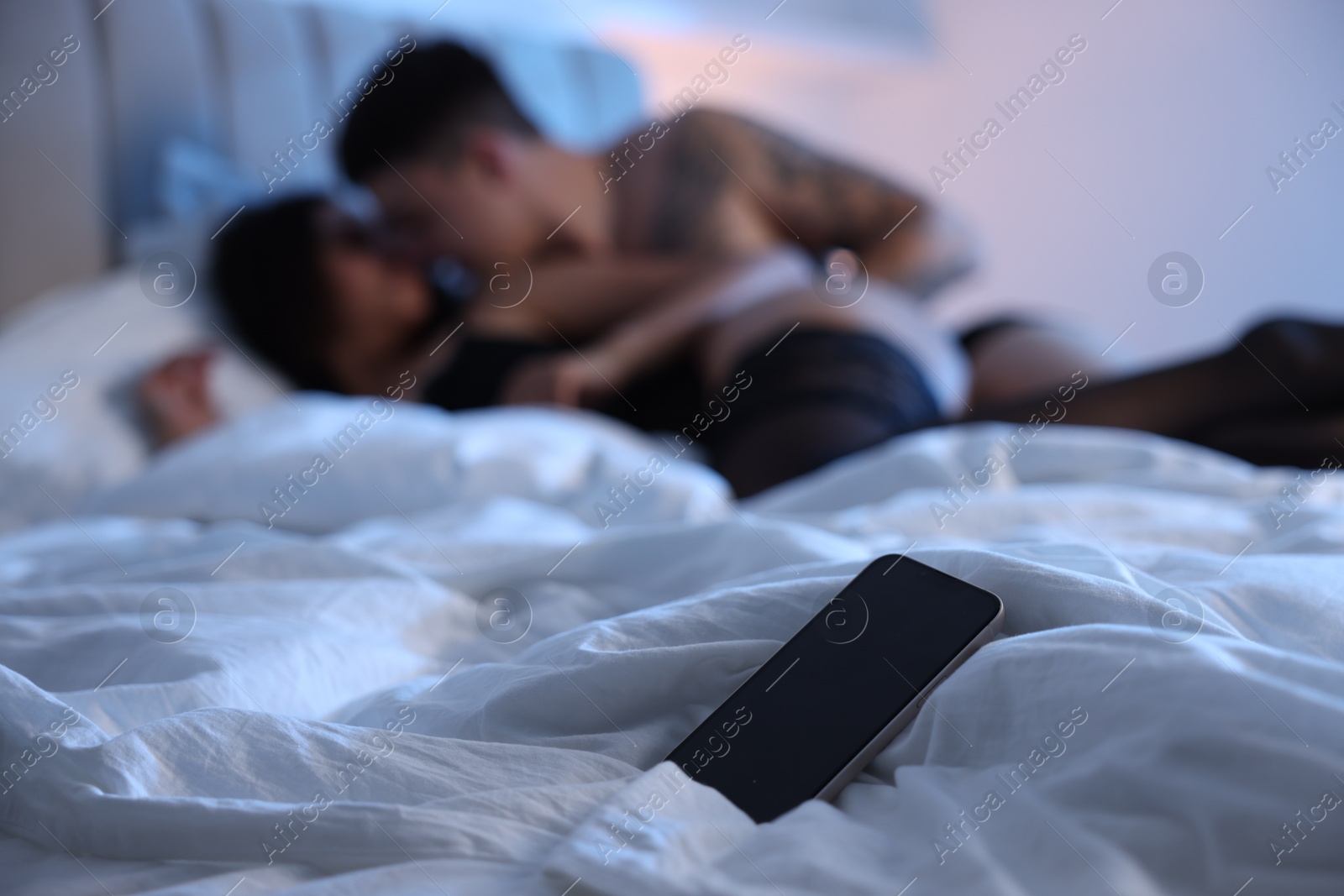 Photo of Betrayal. Passionate lovers having sex on bed, focus on smartphone