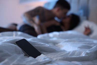 Photo of Betrayal. Passionate lovers having sex on bed, focus on smartphone