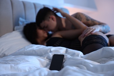 Photo of Betrayal. Passionate lovers having sex on bed, focus on smartphone