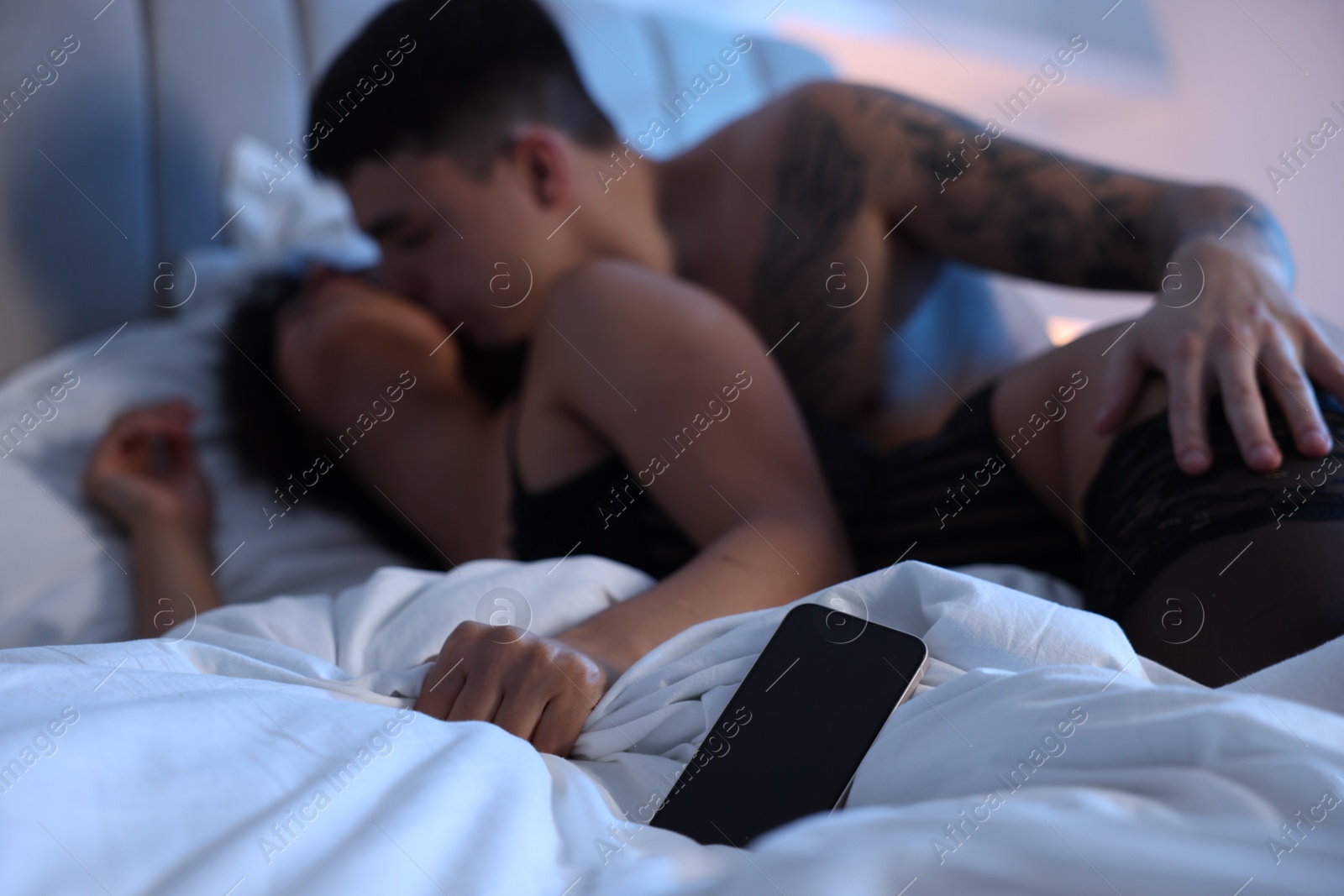 Photo of Betrayal. Passionate lovers having sex on bed, focus on smartphone