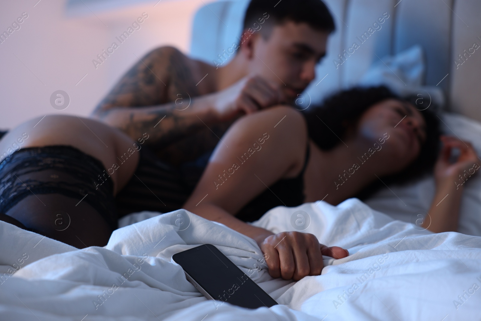 Photo of Betrayal. Passionate lovers having sex on bed, focus on smartphone