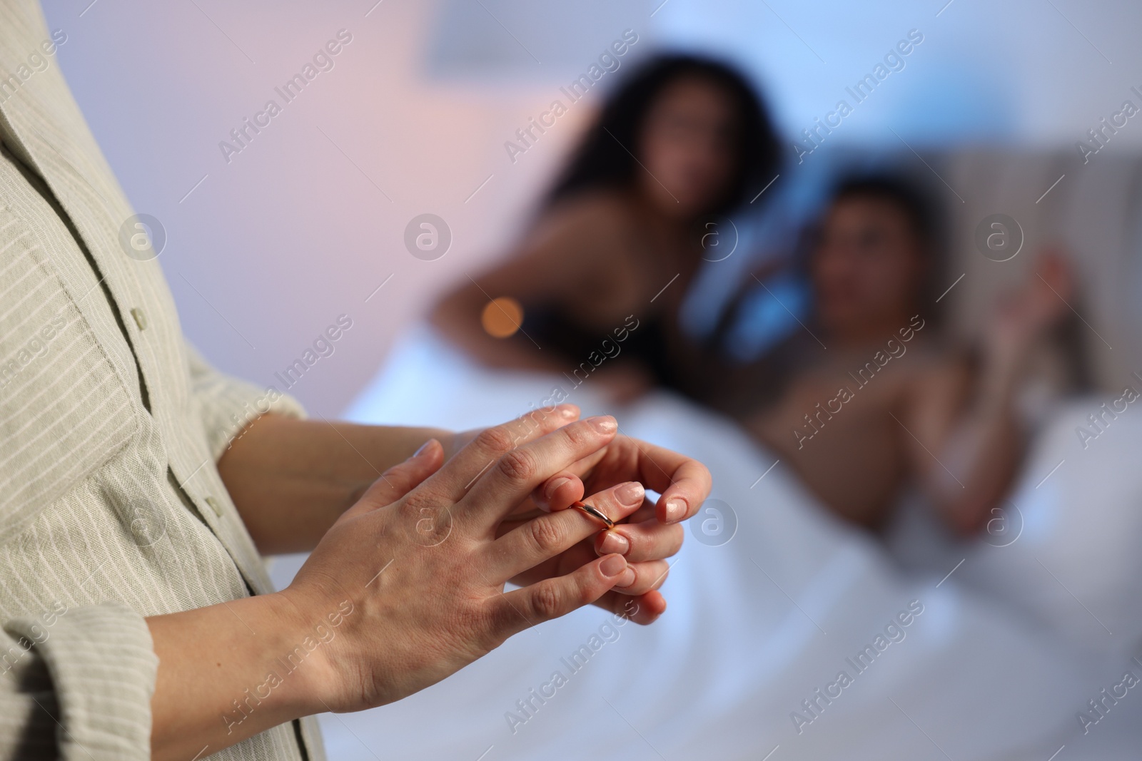 Photo of Betrayal. Wife taking off engagement ring after catching her husband with mistress in bed, selective focus