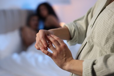 Photo of Betrayal. Wife taking off engagement ring after catching her husband with mistress in bed, selective focus