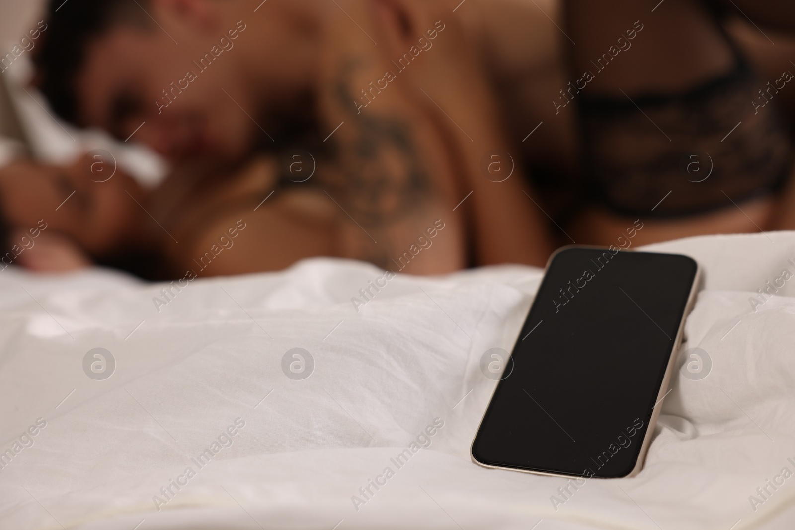 Photo of Betrayal. Passionate lovers having sex on bed, focus on smartphone