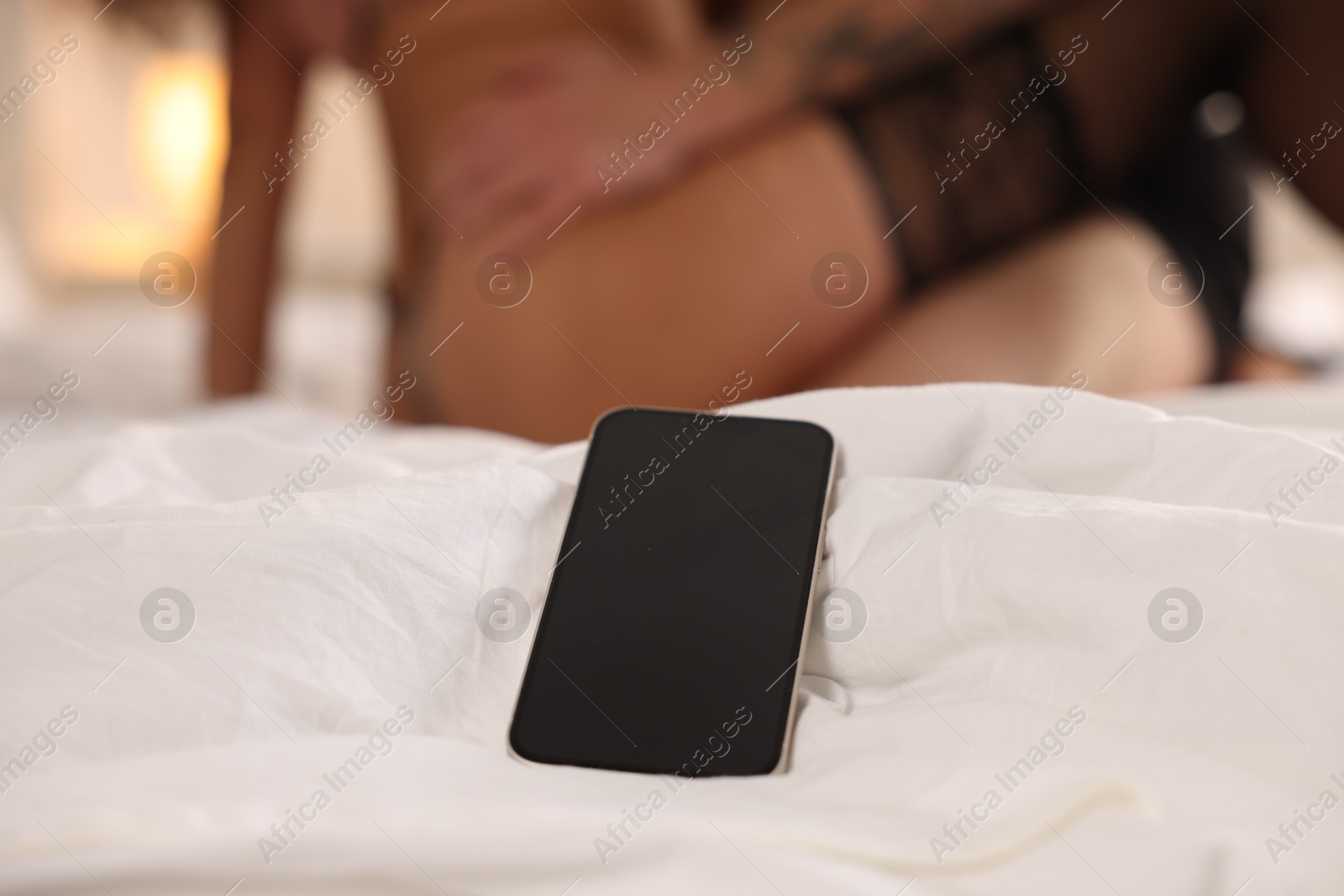 Photo of Betrayal. Lovers having sex on bed, focus on smartphone