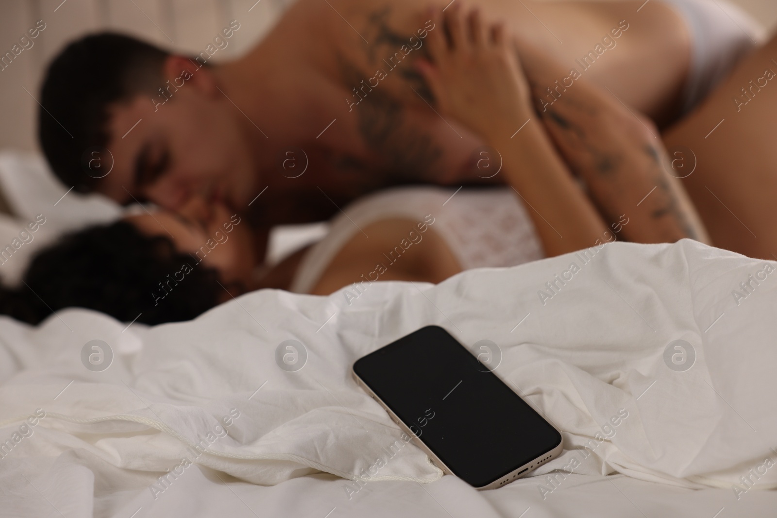 Photo of Betrayal. Passionate lovers having sex on bed, focus on smartphone