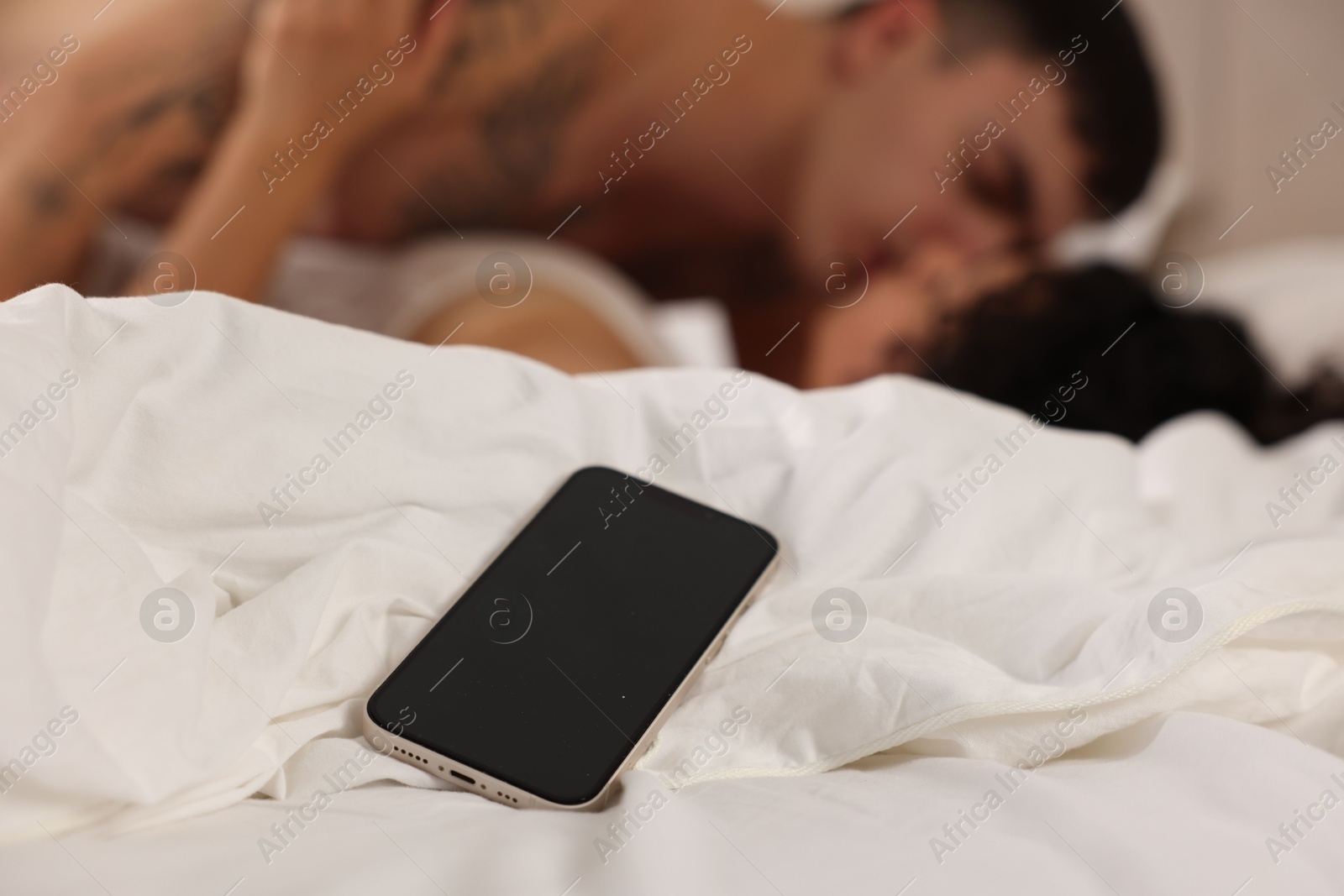 Photo of Betrayal. Passionate lovers having sex on bed, focus on smartphone