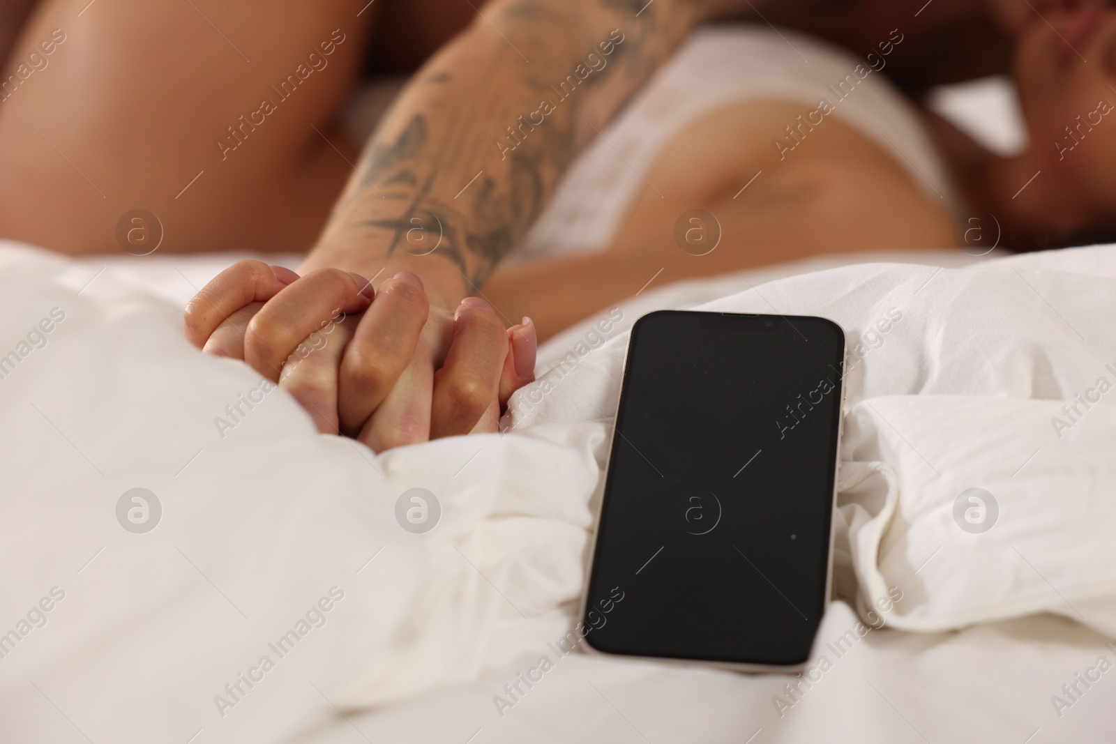 Photo of Betrayal. Lovers having sex on bed, focus on smartphone