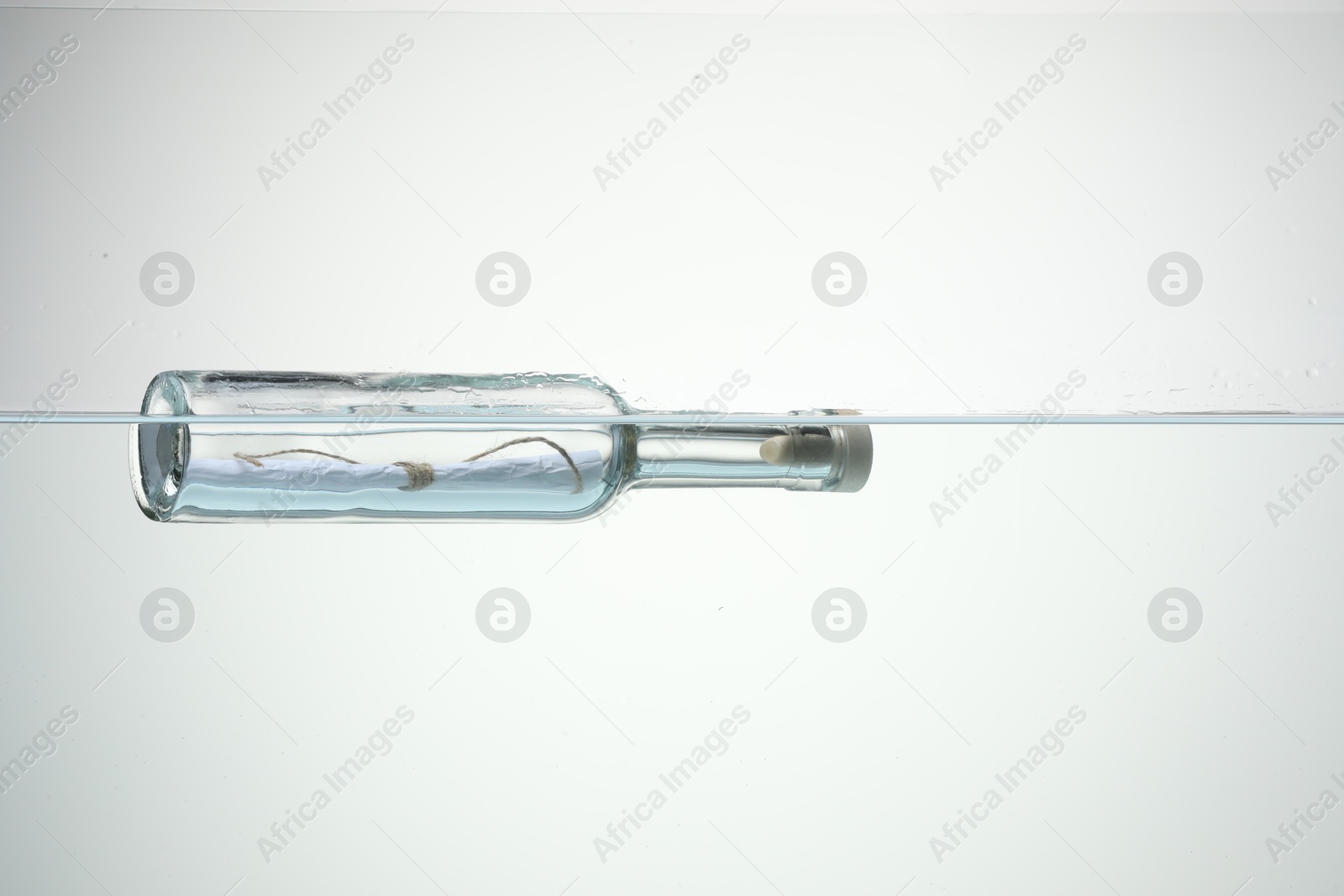 Photo of Corked glass bottle with rolled letter in water on white background