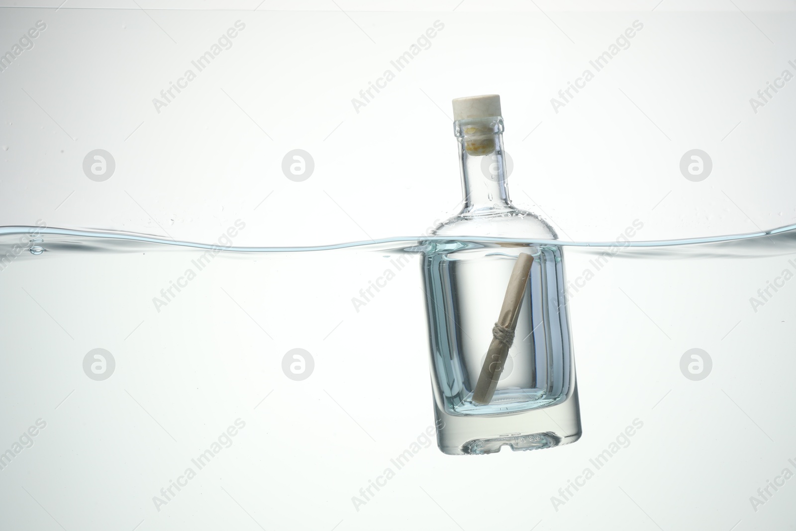 Photo of Corked glass bottle with rolled letter in water on white background