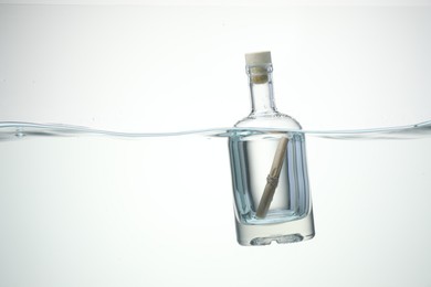 Photo of Corked glass bottle with rolled letter in water on white background