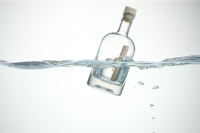 Photo of Corked glass bottle with rolled letter in water on white background