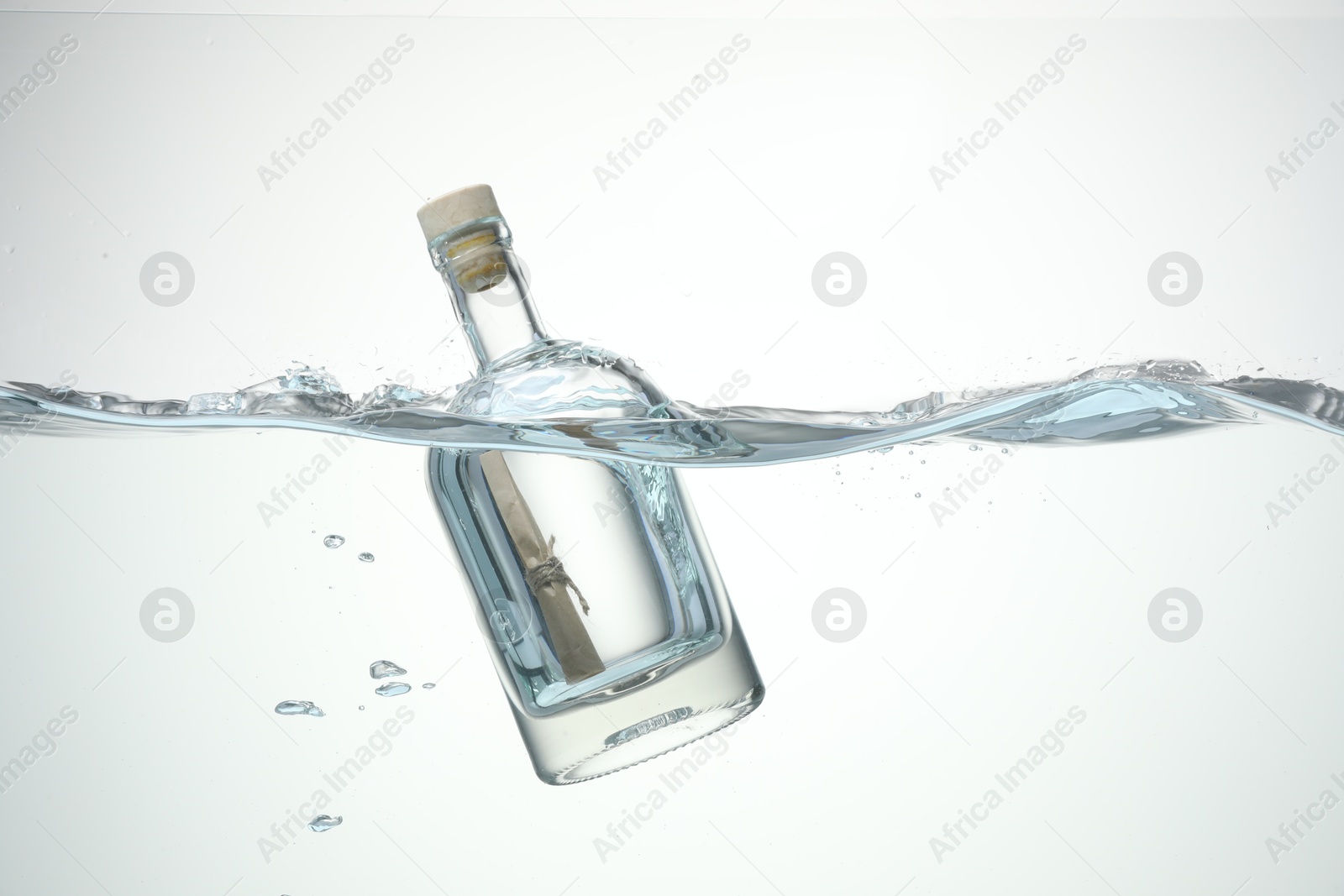 Photo of Corked glass bottle with rolled letter in water on white background