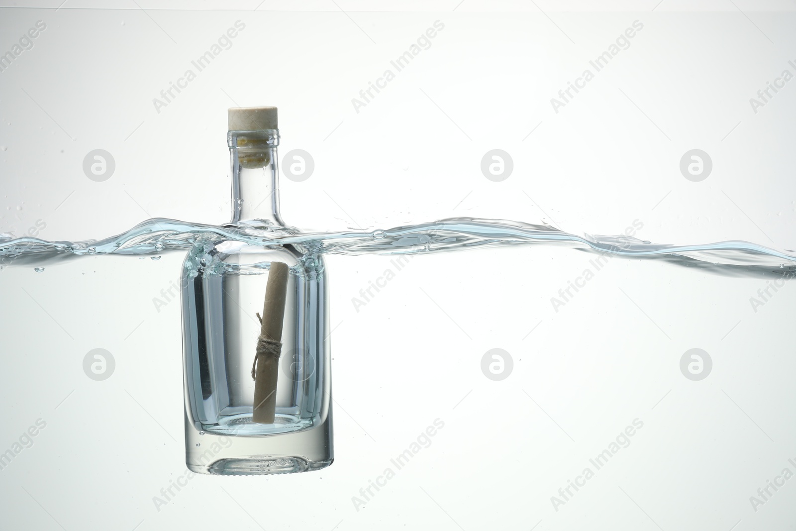 Photo of Corked glass bottle with rolled letter in water on white background