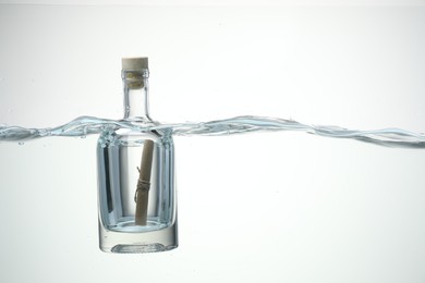 Photo of Corked glass bottle with rolled letter in water on white background