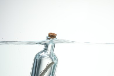 Photo of Corked glass bottle with rolled letter in water on white background