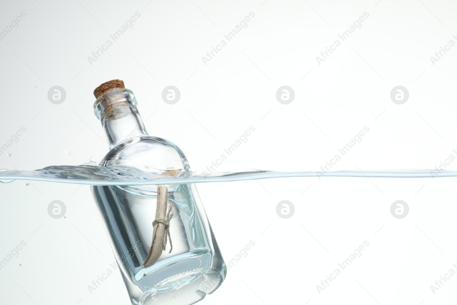 Photo of Corked glass bottle with rolled letter in water on white background