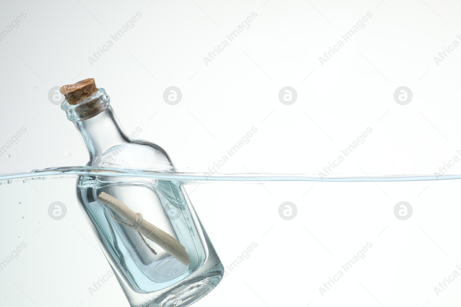 Photo of Corked glass bottle with rolled letter in water on white background