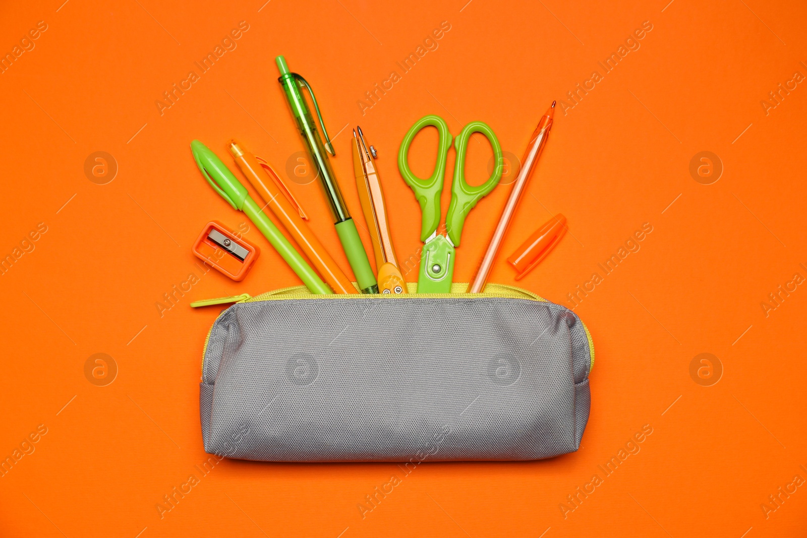 Pencil case and different stationery on orange background, flat lay Photo of Pencil case and different stationery on orange background, flat lay
