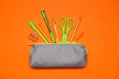 Photo of Pencil case and different stationery on orange background, flat lay