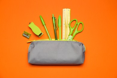 Photo of Pencil case and different stationery on orange background, flat lay