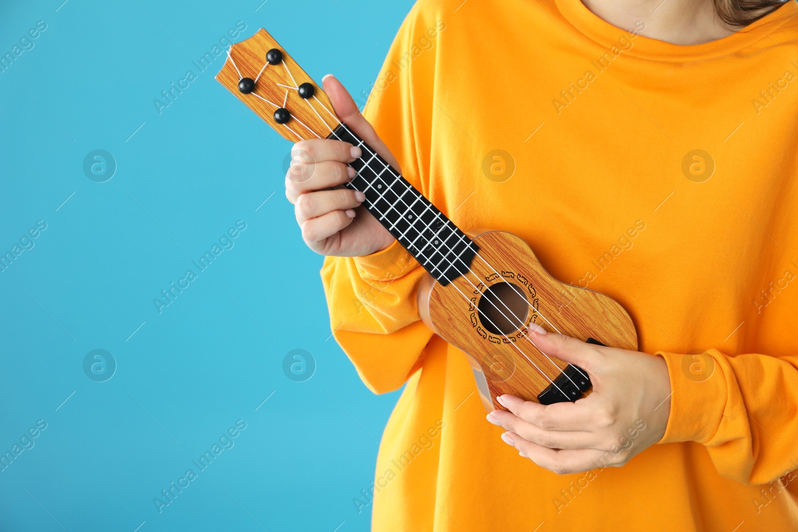 Photo of Woman playing ukulele on light blue background, closeup. Space for text